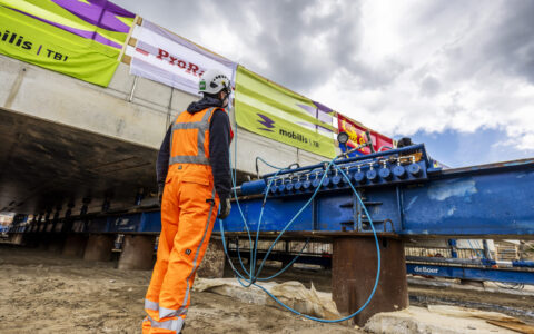 Medewerker staat naast de rails waarover het dak van de onderdoorgang zal schuiven. De rails en betondekken zijn een stuk groter dan de medewerker.