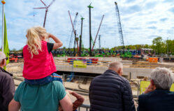 Vader met dochter op de schouders kijken samen naar de werkzaamheden vanaf de kijkerstribune.